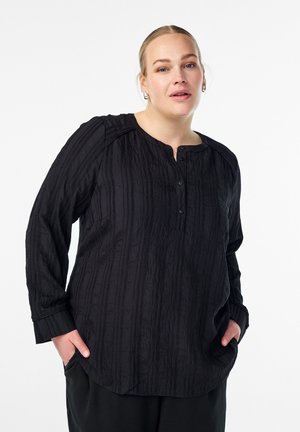 Črna, teksturirana srajca z dolgimi rokavi in ovratnikom tipa crew, z gumbno zadrgo in subtilnimi navpičnimi črtami. Udoben kroj in stranska žepa.