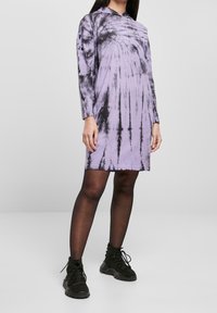 Długa, fioletowa sukienka tie-dye z długim rękawem i luźnym krojem, z okrągłym dekoltem i czarnymi akcentami, zestawiona z czarnymi botkami za kostkę.