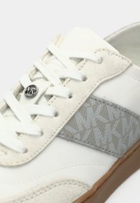 Baskets blanches en suède et cuir, avec un design à lacets, un motif logo gris subtil sur le panneau latéral et une semelle en caoutchouc.