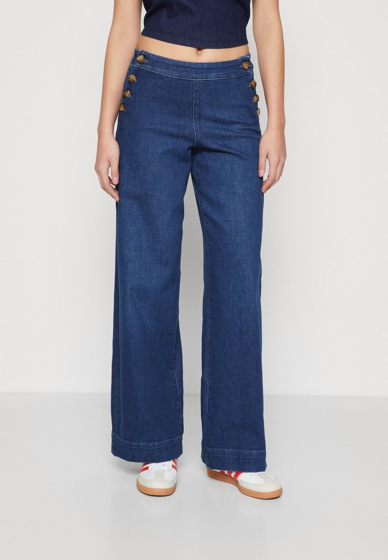 Pantalons en denim à jambes larges bleu foncé, avec une taille haute et six boutons décoratifs sur le côté gauche. Texture lisse, design décontracté.