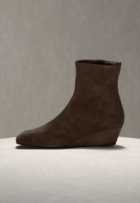 Bottine en daim marron avec un petit talon compensé, présentée sur une surface claire avec un fond neutre.
