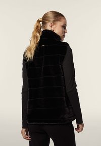 Musta tekoturkisliivi vertikaaliruuduilla, korkea kaulus ja sivutaskut, käytetään mustan pitkähihaisen paidan päällä. Sujuva pinta.