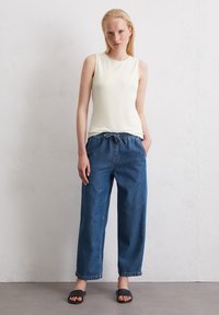 Wit mouwloos topje gecombineerd met losse, donkerblauwe denim broek en zwarte instappers. Eenvoudig ontwerp met elastische tailleband.