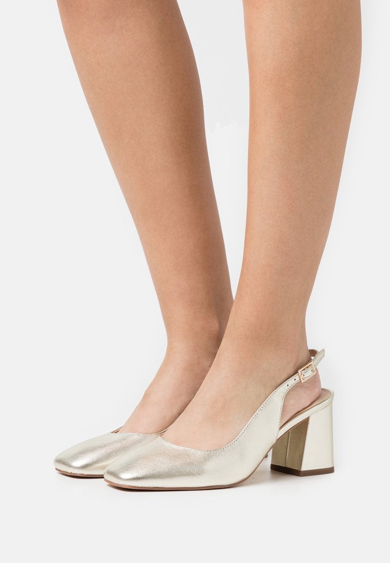 Escarpins dorés métalliques à bride arrière avec un bout arrondi, un talon bloc de hauteur moyenne et un détail de couture subtil sur les côtés. Texture lisse et brillante.