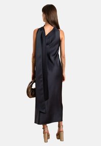Schwarzes Satin-Kleid mit einer Rückenknoten-Detail. Es hat eine eleganten, taillierten Silhouette und einen knielangen Saum. Getragen mit einer strukturierten Tasche und Plateausandalen.