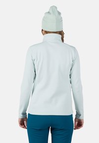 Lyseblå fleecejakke med høj krave, lange �ærmer og en glat tekstur, parret med teal bukser og en matchende strikket hue.