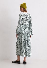 Langärmliges, gestuftes Kleid aus hellblauem Stoff mit schwarzem Blumenmuster. Kombiniert mit einer Senfgelben Strickmütze und schwarzen Schuhen.