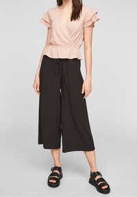 Top rosa con mangas con volantes, combinado con pantalones negros de pierna ancha. La modelo lleva sandalias planas negras. La tela parece ligera y texturizada.