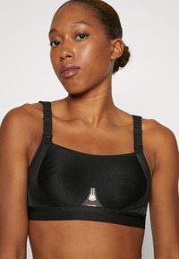 Top sportivo nero realizzato in tessuto testurizzato con spalline regolabili, caratterizzato da un dettaglio del logo decorativo sul davanti e una finitura liscia.