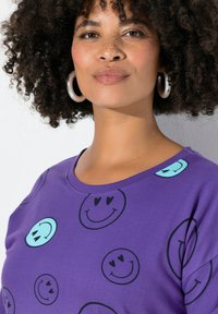 Paars T-shirt met korte mouwen met zwarte en lichtblauwe smileygezichten. Gemaakt van zachte stof met een ronde halslijn en een ontspannen pasvorm.