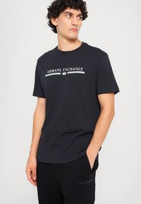 Svart bomull T-skjorte med "Armani Exchange"-logo i hvitt og lyseblått. Korte ermer, klassisk rund hals-design, glatt tekstur.
