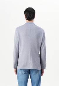 Blazer da uomo in una fantasia a quadri blu chiaro e bianco, con un solo spacco e vestibilità su misura, abbinato a jeans in denim blu chiaro.
