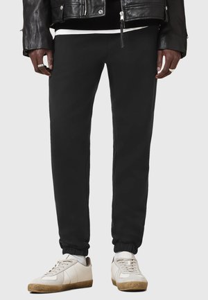 Schwarze Fleece-Jogginghosen mit elastischem Bund und Bündchen, kombiniert mit off-white Sneakers mit beigen Akzenten und einem grauen Einsatz.