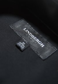 Zwarte stoffen label met "LINDBERGH" in witte letters opgedrukt. Aanvullend etiket zichtbaar met zorgsymbolen en nummer 3570.