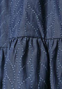 Detail blízkého záběru na modrou látku s texturovaným cikcakovým prošíváním a nabíraným švem.