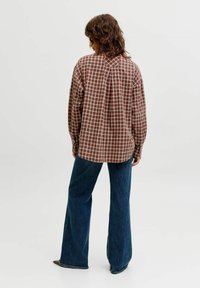 Rdeča in rjava karirana srajca z dolgimi rokavi, sproščenega kroja, skupaj z modrimi razširjenimi kavbojkami, nošena od zadaj. Gladek tekstura tkanine.