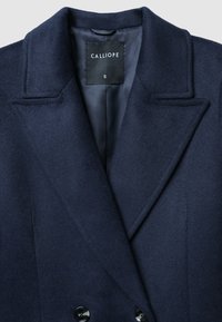 Cappotto in misto lana blu navy con design doppiopetto, revers a punta e bottoni neri. Presenta una fodera in raso liscia e un'etichetta di misura.