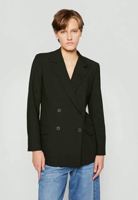 Černý dvouřadý blazer s klopami, dvěma předními kapsami a knoflíkovými detaily, spárovaný se světle modrými džíny.