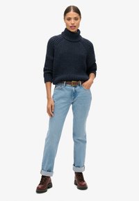 Granatowy sweter z golfem z dzianiny o prążkowanej fakturze, w połączeniu z jasnoniebieskimi podwiniętymi dżinsami i brązowymi botkami na sznurowadła.