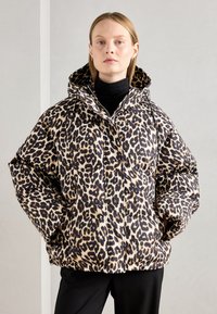 Chamarra tipo puff en estampado de leopardo con capucha, que presenta un diseño grueso y acolchado en tonos beige y negro. Detalles de cremallera y bolsillos laterales.