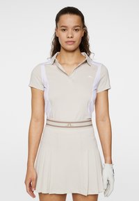 Beige golfpolo med vita sidodetaljer, kort ärm och krage. Matchas med en beige plisserad kjol och en vit golfhandske.