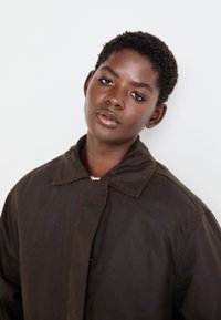 Veste oversize marron avec un col structuré et une fermeture à boutons. Texture lisse, avec un design simple et un style minimaliste.