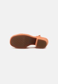 Semelle de chaussure en daim orange avec motif antidérapant texturé, talon léger et avant lisse et arrondi. Design épuré avec peu d'éléments métalliques.