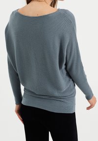 Jasnoniebieski sweter prążkowany o luźnym kroju, szerokim dekolcie i długich rękawach. Posiada teksturowany materiał oraz dopasowany pas w talii.