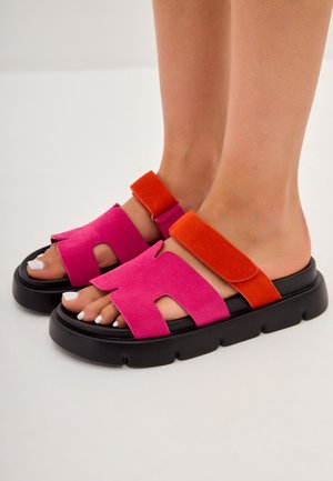 Sandales ouvertes avec des dessus en daim rose et orange, présentant des découpes et des sangles ajustables, montées sur une épaisse semelle noire.