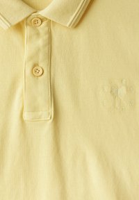 Ljusgul polo skjorta tillverkad av strukturerat tyg med en treknappslåsning och en broderad palmträdslogotyp på bröstet.