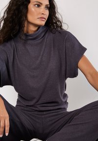 Überdimensioniertes, dunkelgraues Strickoberteil mit Stehkragen, lässigem Schnitt, kurzen Ärmeln und weicher Textur, kombiniert mit passenden dunkelgrauen Hosen.