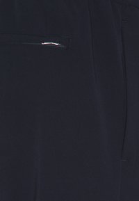Navy fabric with a smooth texture, featuring a close-up of a side pocket, finished with a minimalist silver zipper detail.