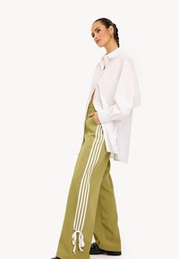 Witte, oversized button-up blouse gecombineerd met hooggewaadde, wijduitlopende olijfgroene broek met drie witte strepen en strikdetails bij de enkels.