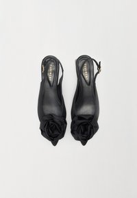 Tacones slingback negros de satén, con punta afilada y una gran decoración de rosa de tela en la parte delantera. Textura suave y diseño elegante.