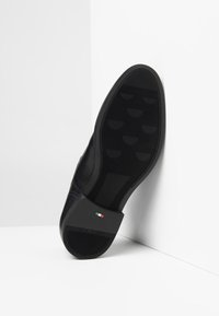 Semelle de chaussure en cuir noir avec une surface texturée, dotée d'un embout de talon rectangulaire et d'un petit accent de drapeau italien à l'arrière.