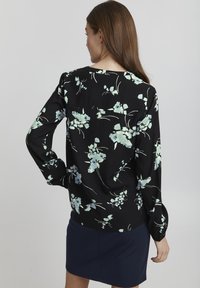 Svart blus med ljusblå blommönster, långa ärmar och avslappnad passform. Har en rund halsringning och en mjuk, smooth textur.