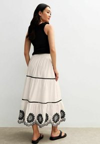 Witte gelaagde rok met zwarte bloemenborduursel langs de zoom en zwarte accenten; gecombineerd met een strakke zwarte top en sandalen.