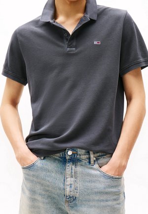 Ciemnoszara koszulka polo z teksturowanej tkaniny i krótkimi rękawami, z małym logo. W połączeniu z jasnoniebieskimi jeansami z denimu.