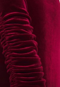 Tissu en velours rouge profond avec une texture froncée rassemblée créant de doux plis horizontaux le long de la surface.