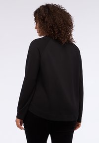 Czarna bluza z luźnym krojem, rękawami raglanowymi i okrągłym dekoltem. Wykonana z miękkiego materiału o gładkiej fakturze.
