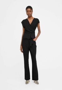 Top avvolgente nero con maniche corte e cintura in vita, abbinato a pantaloni neri a zampa e tacchi con stampa serpente. Tessuto morbido con design elegante.