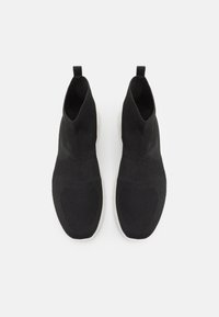 Sneaker nere in maglia alte fino alla caviglia con superficie testurizzata, dotate di una linguetta e una suola bianca a contrasto. Design minimalista con forma affusolata.