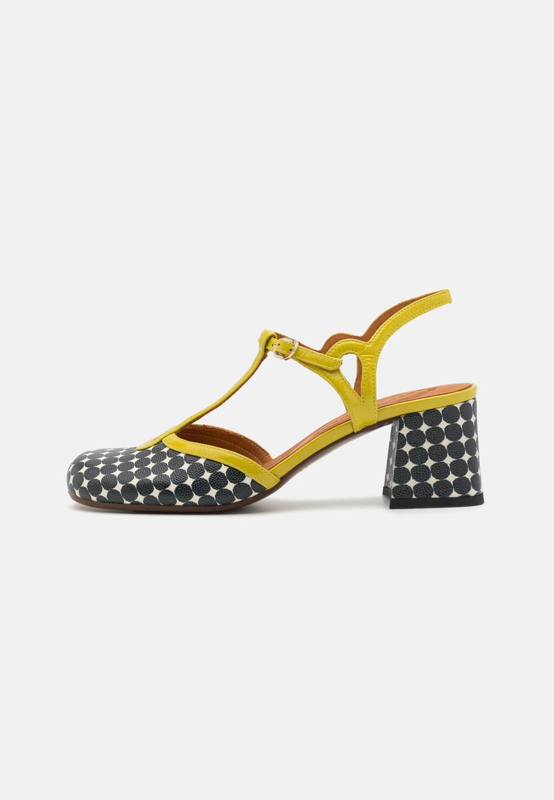 Kollane ja mustade täppidega slingback kingad ümmarguse toe, nähtava kontsaga, T-riba disainiga ja tekstuursete materjalidega. Kummist tald ja aktsentdetailid.