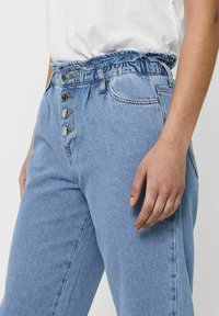 Light blue denim jeans with a relaxed fit, high waist, and an elastic waistband. Features five buttons and front pockets.