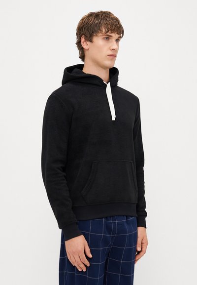 Μαύρο φλις φούτερ με μπροστινή τσέπη καγκουρό, ρυθμιζόμενο λευκό κορδόνι και ραμμένες μανσέτες. Φοριέται με μπλε καρό παντελ�όνι.