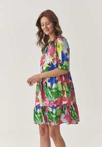 Bloemige jurk met korte mouwen, versierd met een levendig patroon van roze, blauwe en groene bloemen. Kenmerkt zich door een vloeiende zoom en een zachte textuur.
