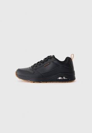 Black Skechers sneaker with lace-up front, visible air cushion in sole, and brown pull tab and sole accents on a plain background.