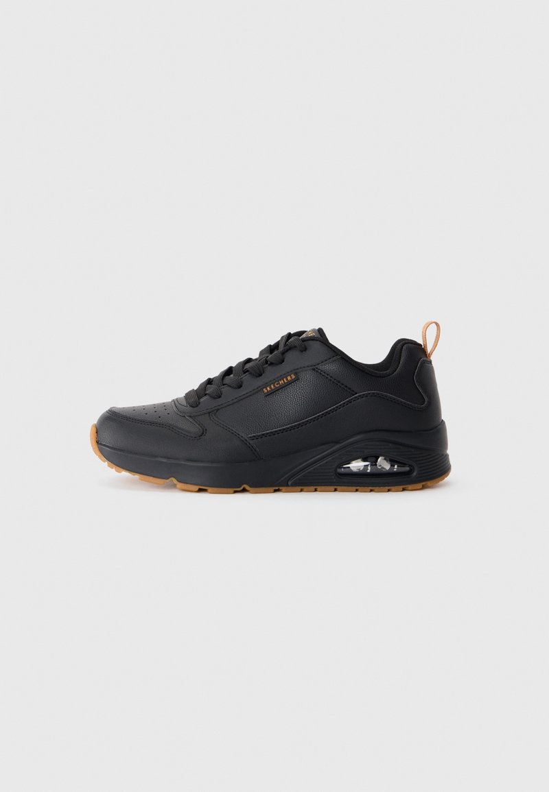 Baskets Skechers noires avec lacets à l'avant, coussin d'air visible dans la semelle et languette ainsi que détails marron sur la semelle, sur fond uni.