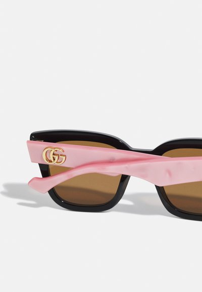 Lunettes de soleil noires avec verres marron, forme carrée plate, branches en acétate rose avec un détail logo GG doré.