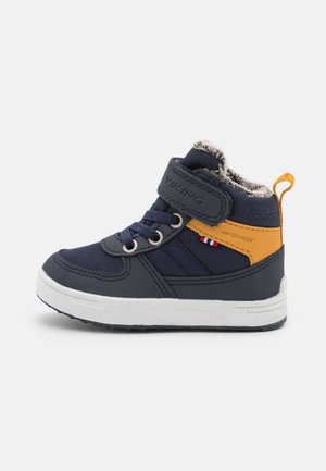 Baskets imperméables pour enfants bleu et jaune avec semelle blanche, fermeture Velcro, lacets et doublure en fourrure vues de côté sur fond blanc.